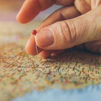 Eine Hand steckt einen Pin in eine Landkarte.